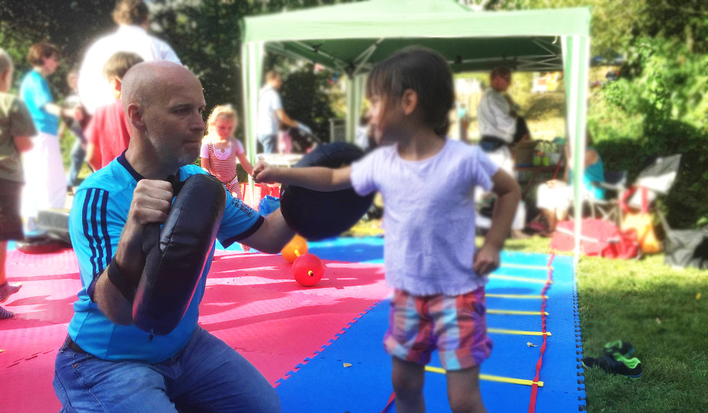 Karateka mit Kind bei Fauststoß-Übung mit Pratzen auf der Mattenfläche am Karate-Stand in Montabaur